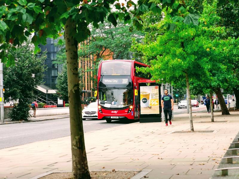 A red double-decker bus on a tree-lined street with pedestrians on the pavement