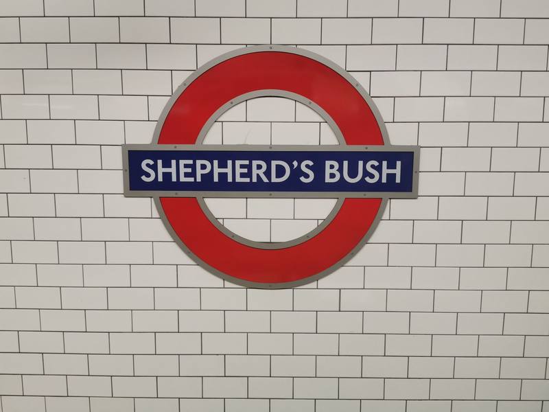 The red and blue Shepherd's Bush Underground roundel on a white tiled wall